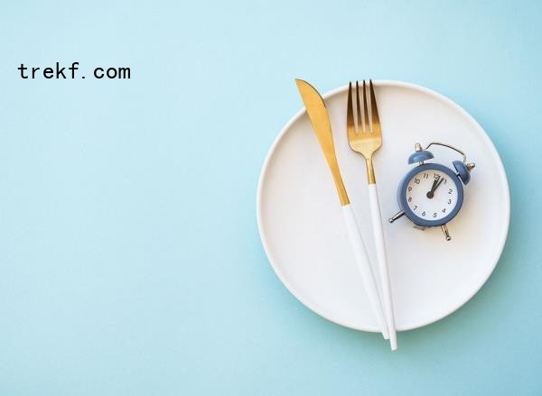 Empty plate, fork and knife, and an alarm clock on blue background